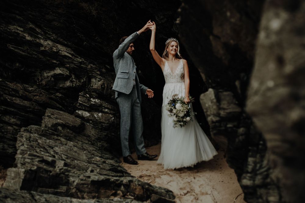 Newlyweds share a joyful moment while standing on dramatic rocky cliffs.