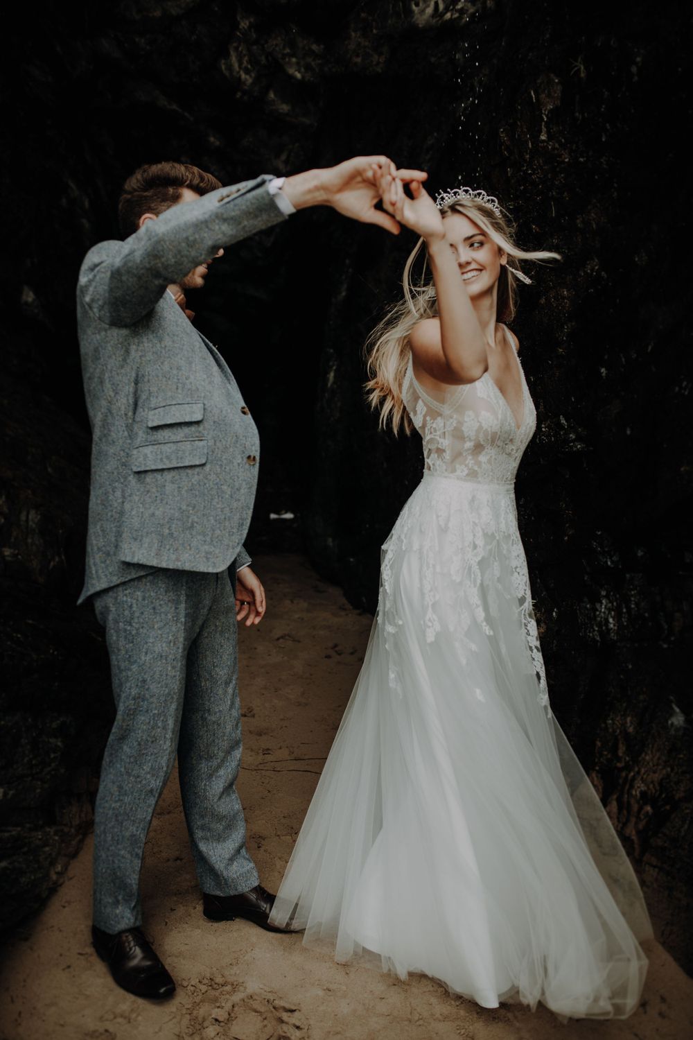A couple dancing joyfully together outdoors, with the bride in a flowing white dress and groom in a gray suit.