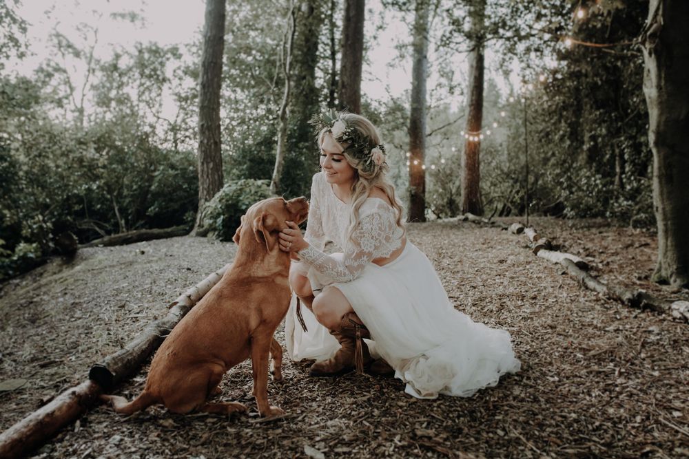 A golden retriever sits with someone in a white dress in a wooded outdoor setting.