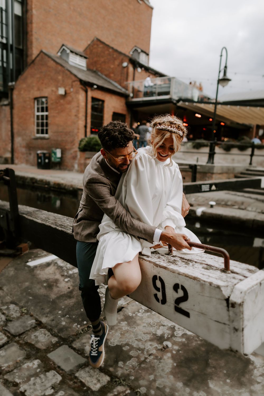 A romantic moment shared between a couple sitting on a canal wall in an urban setting.