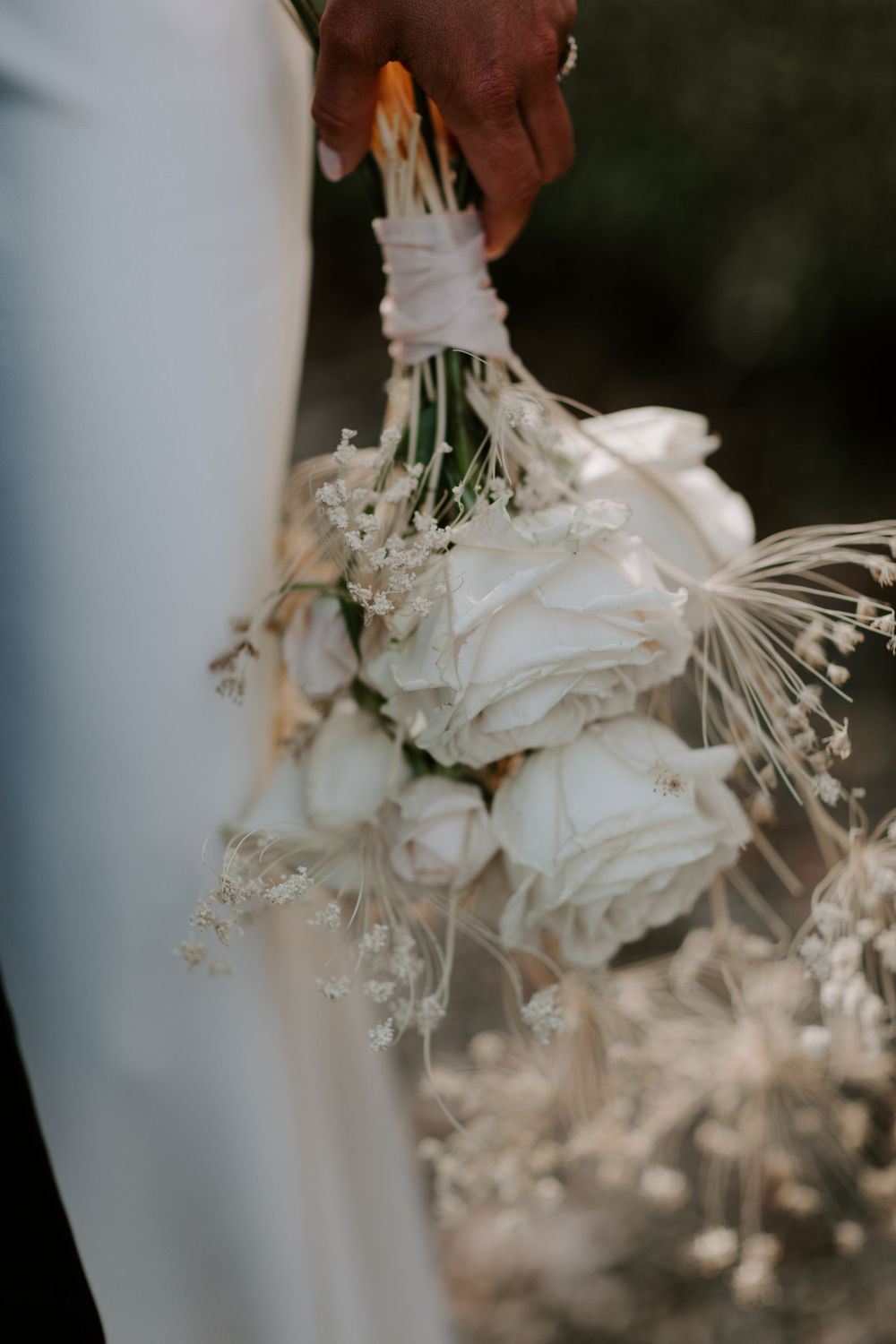 Close-up of white roses and baby's breath wedding bouquet held against white dress.
