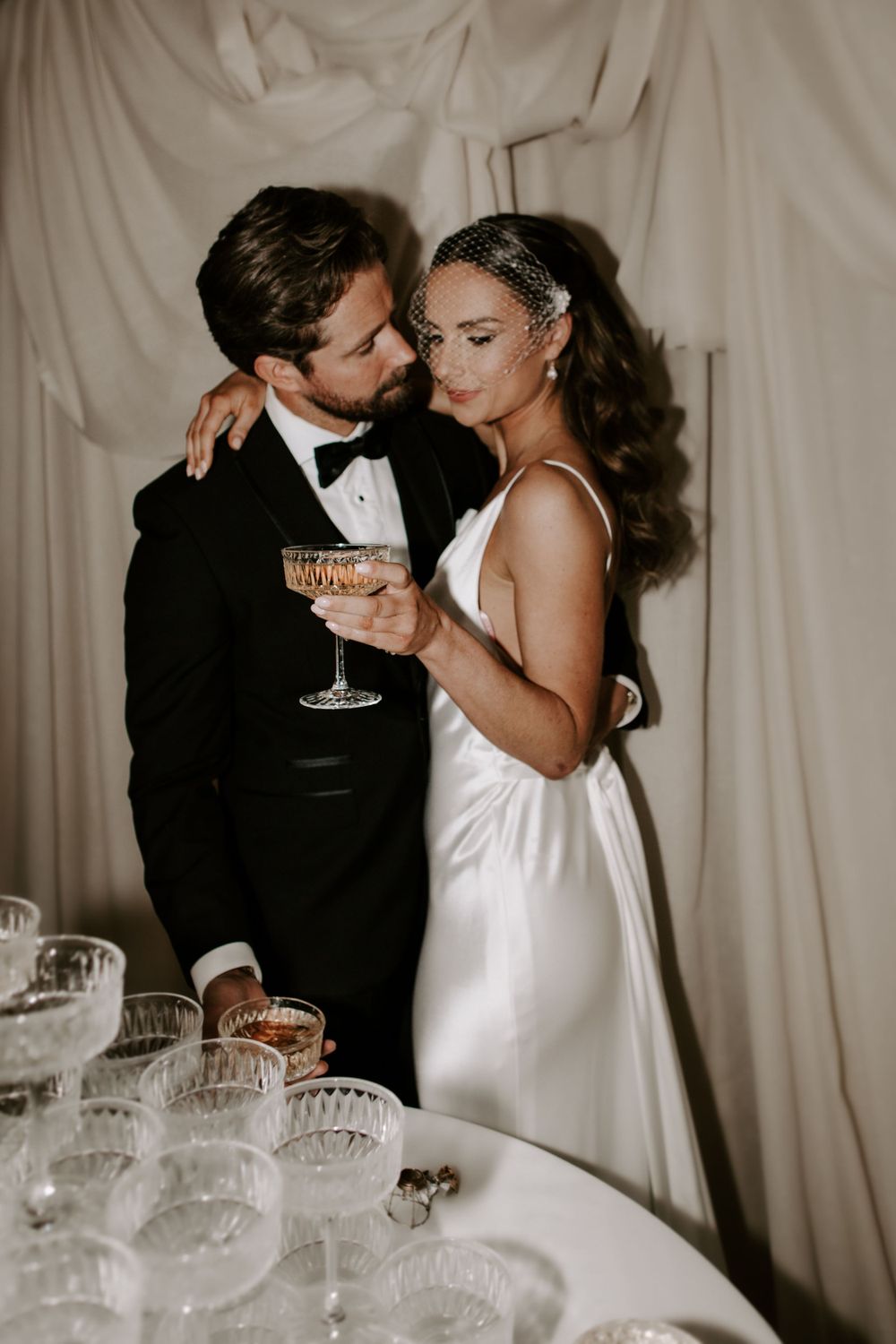 An elegant couple shares an intimate moment with champagne at their wedding reception.
