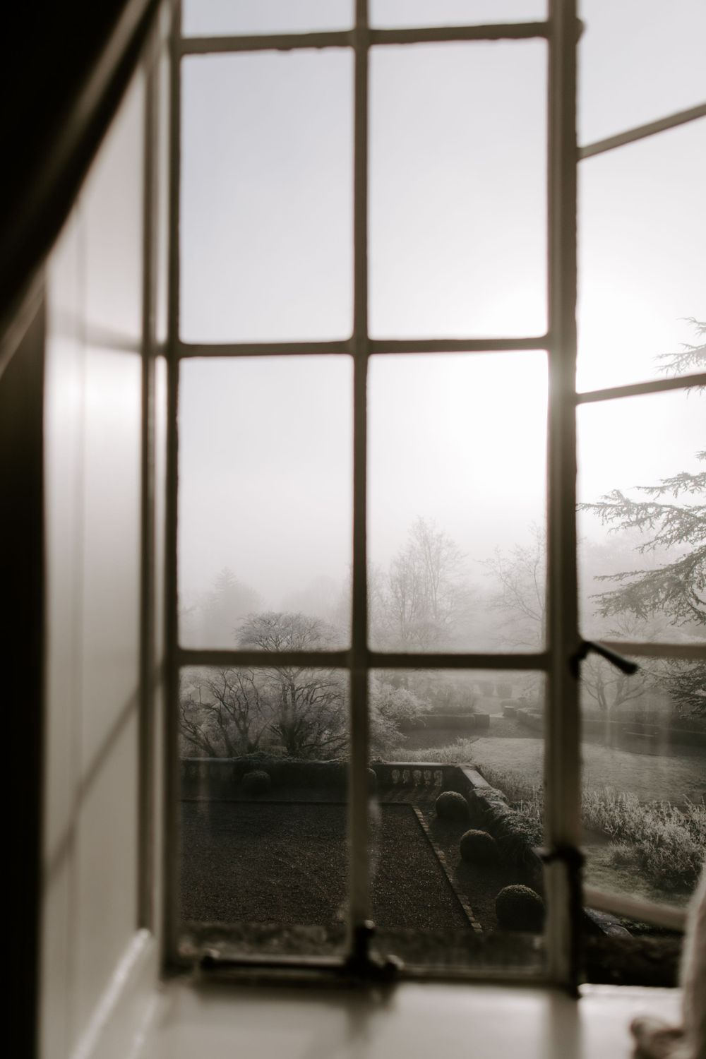 Foggy landscape view through vintage window panes creating a moody atmospheric scene.
