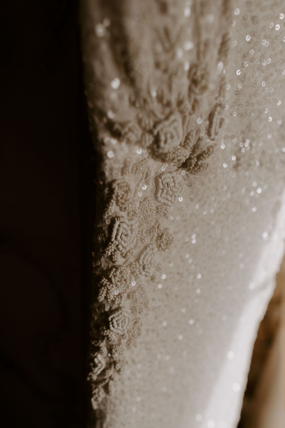 Close-up detail of delicate lace and beading on white wedding dress fabric.
