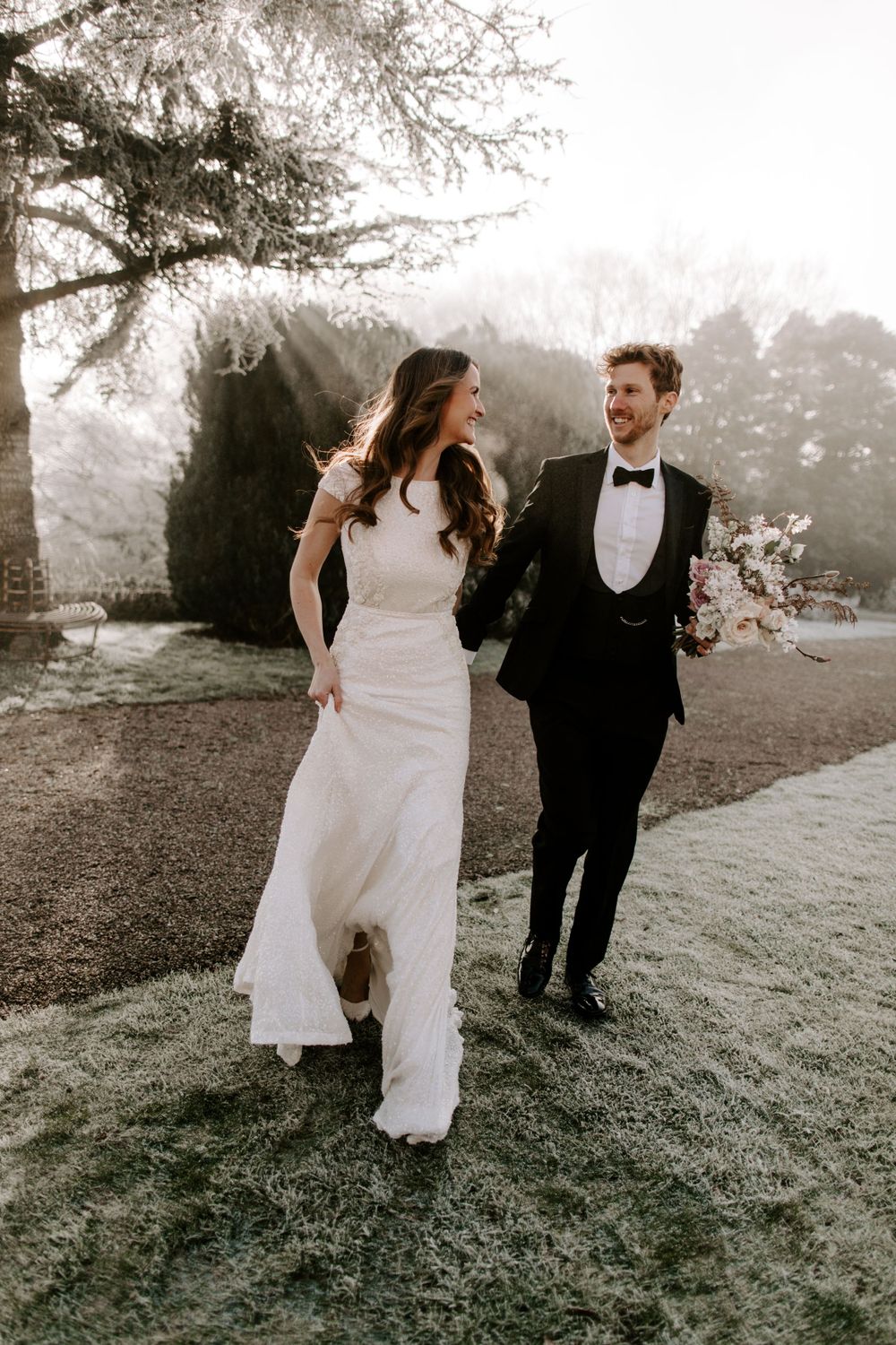 Wedding couple walking and laughing together on misty grounds with elegant attire.