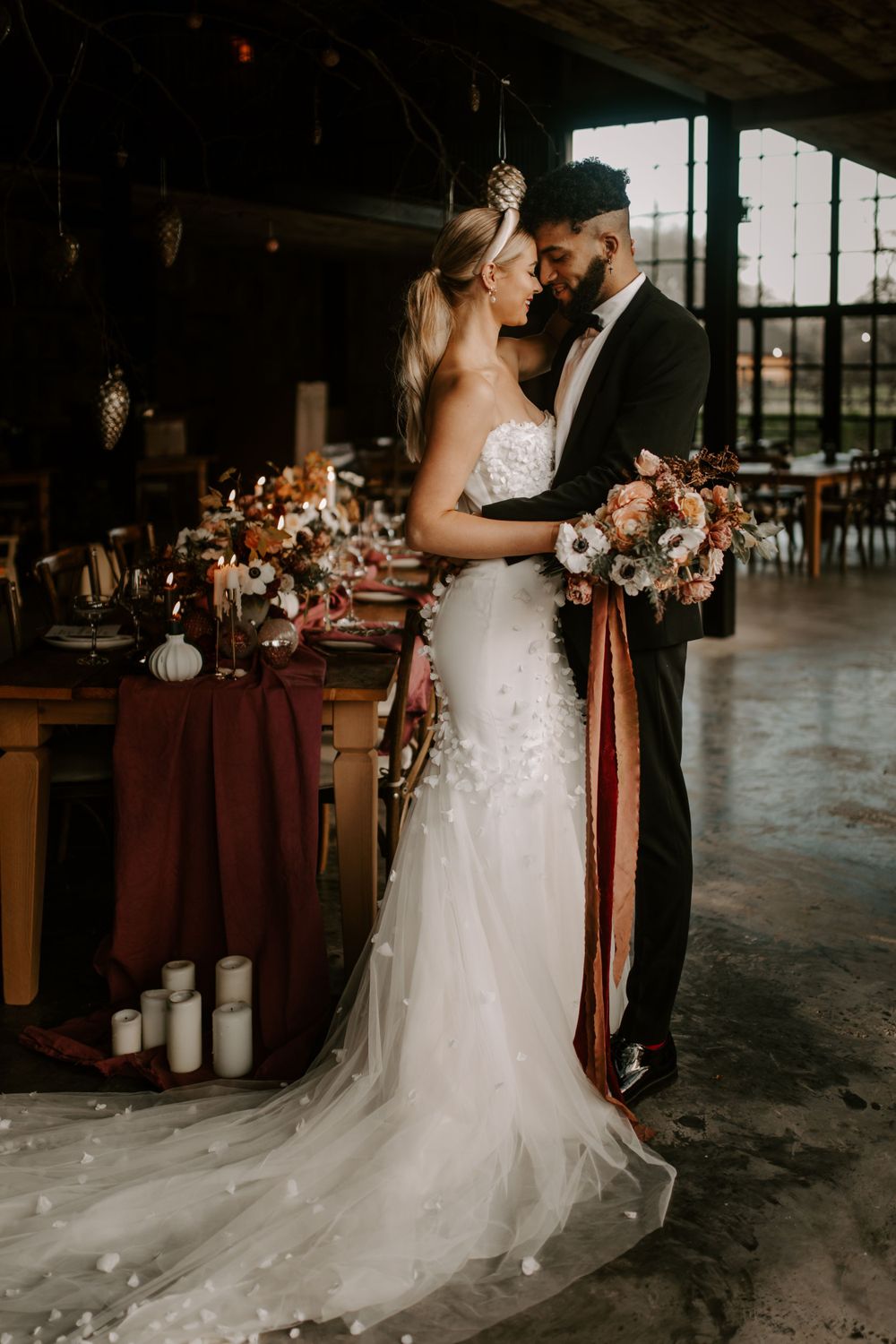 A couple embraces in an industrial venue with romantic table settings and decor.