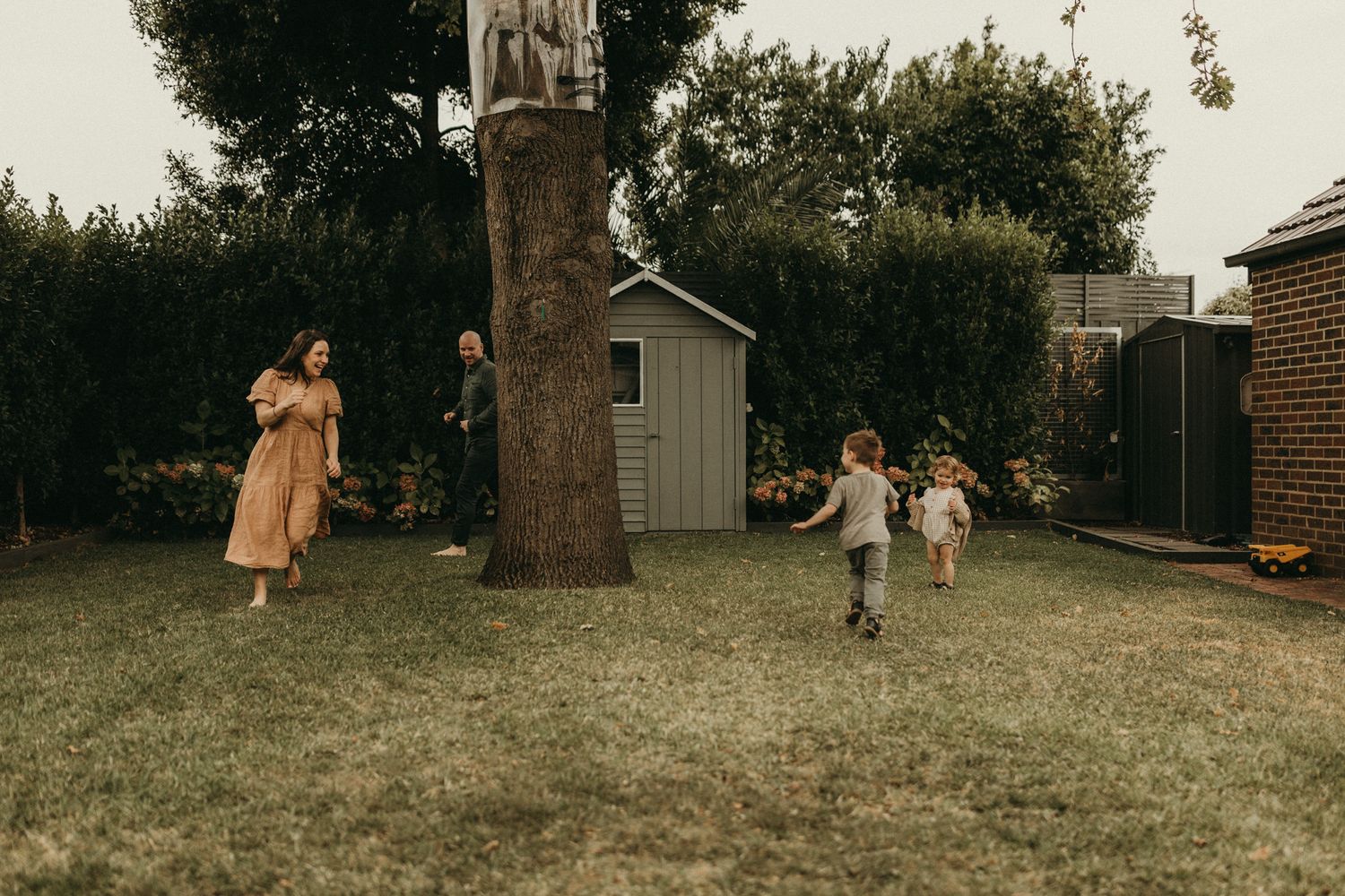 Children playing in a backyard near a garden shed on an overcast day.