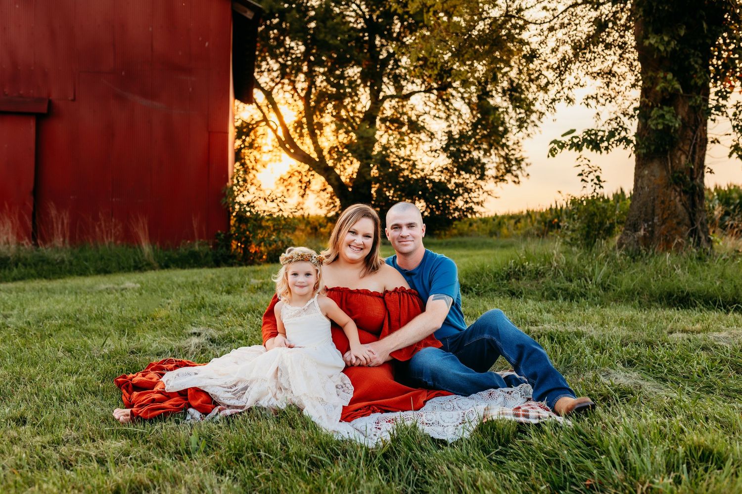 A family relaxes on a picnic blanket near a red barn during golden hour.