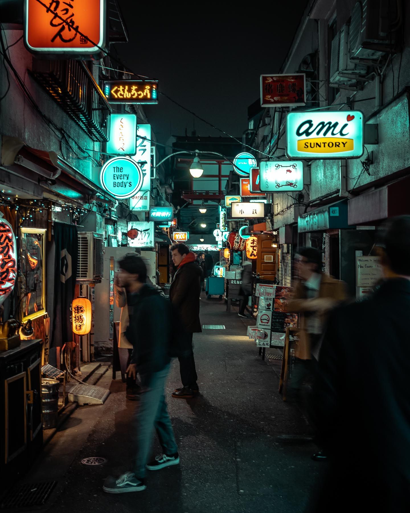 Narrow alley in Japan filled with neon signs and restaurant entrances at night.