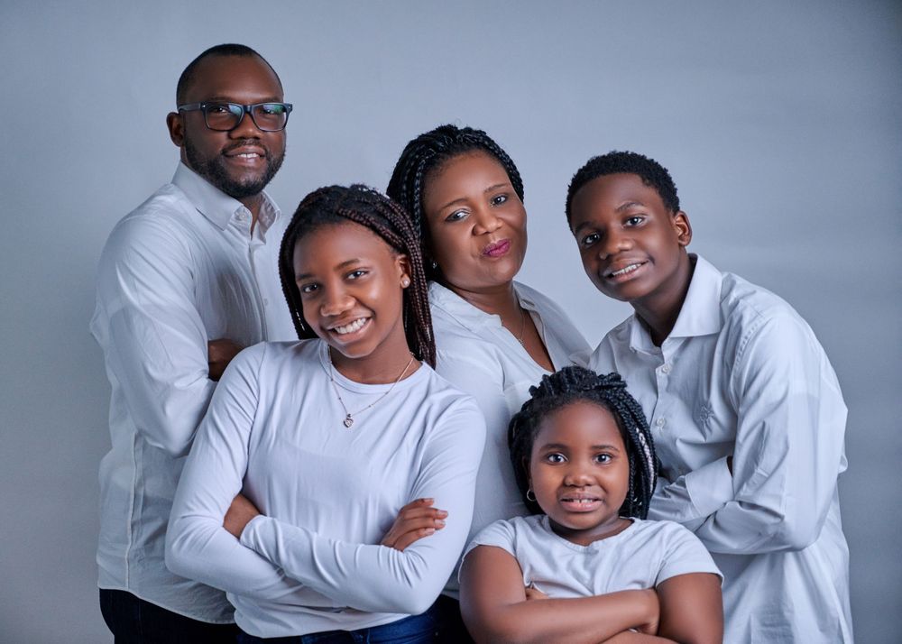 Family of five wearing coordinated white outfits pose together for studio portrait.