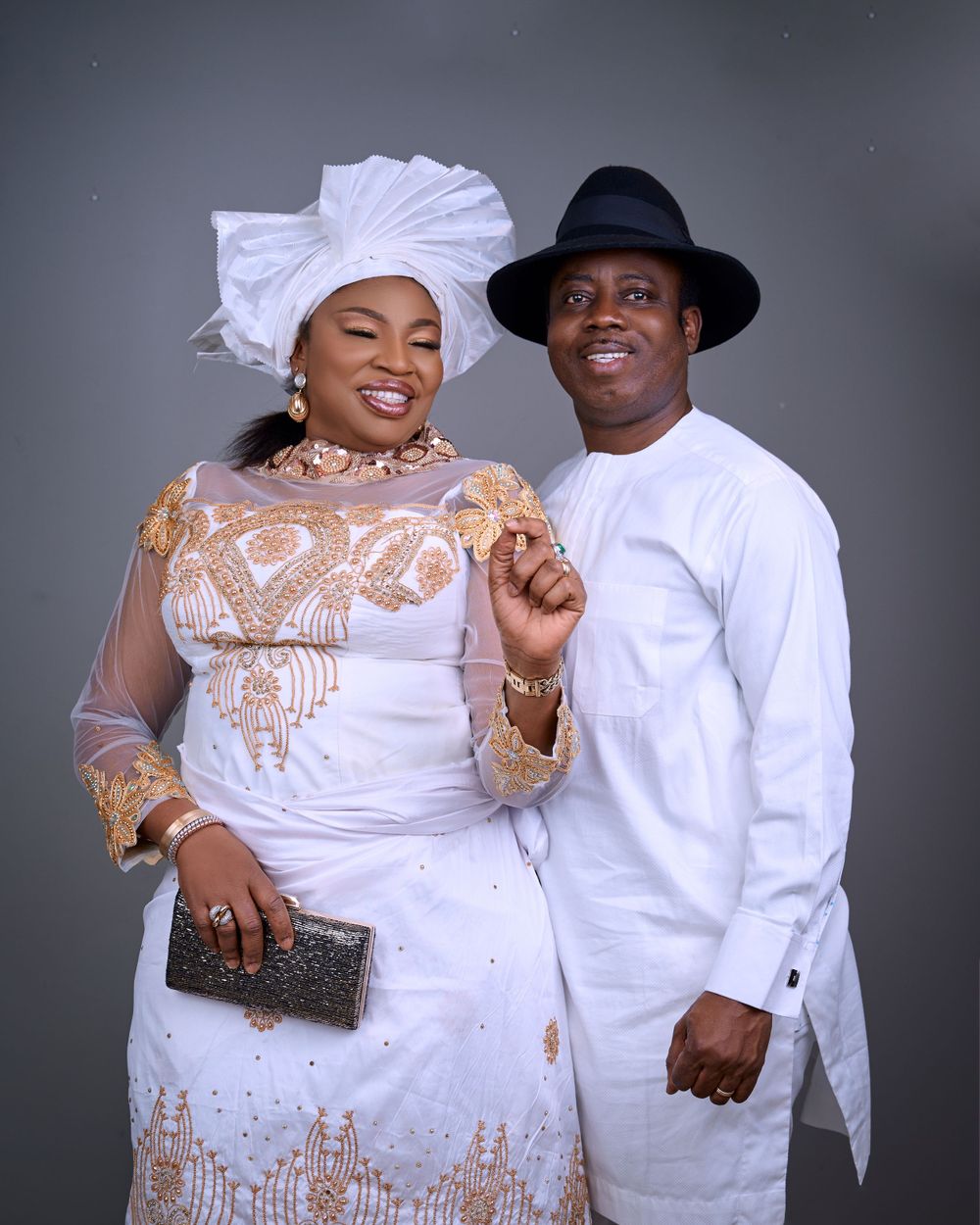 Couple in traditional white and gold attire pose together for formal portrait.
