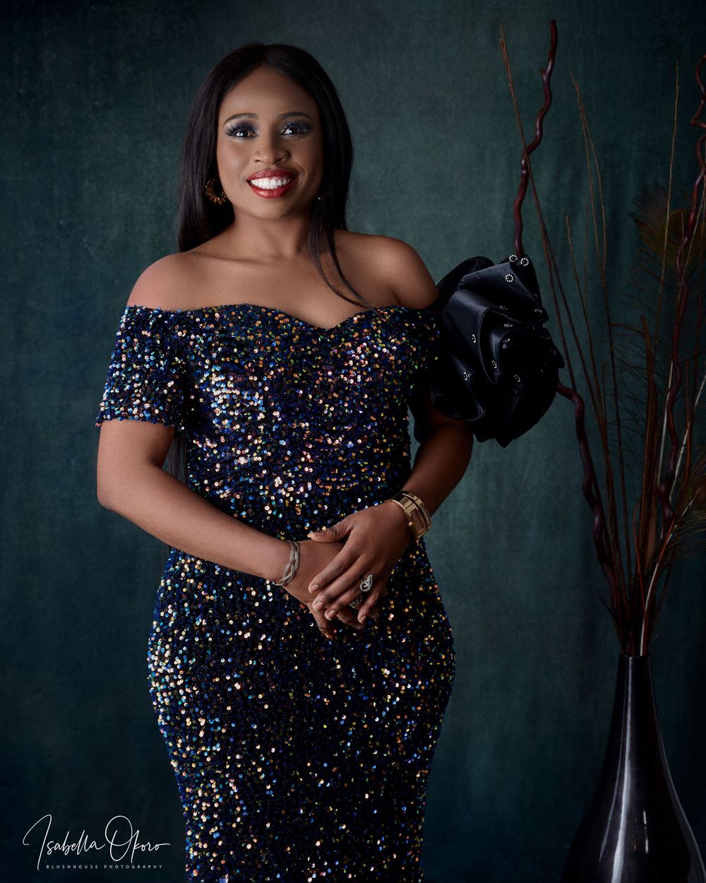 Portrait of woman in off-shoulder sequined dress against dark green background.