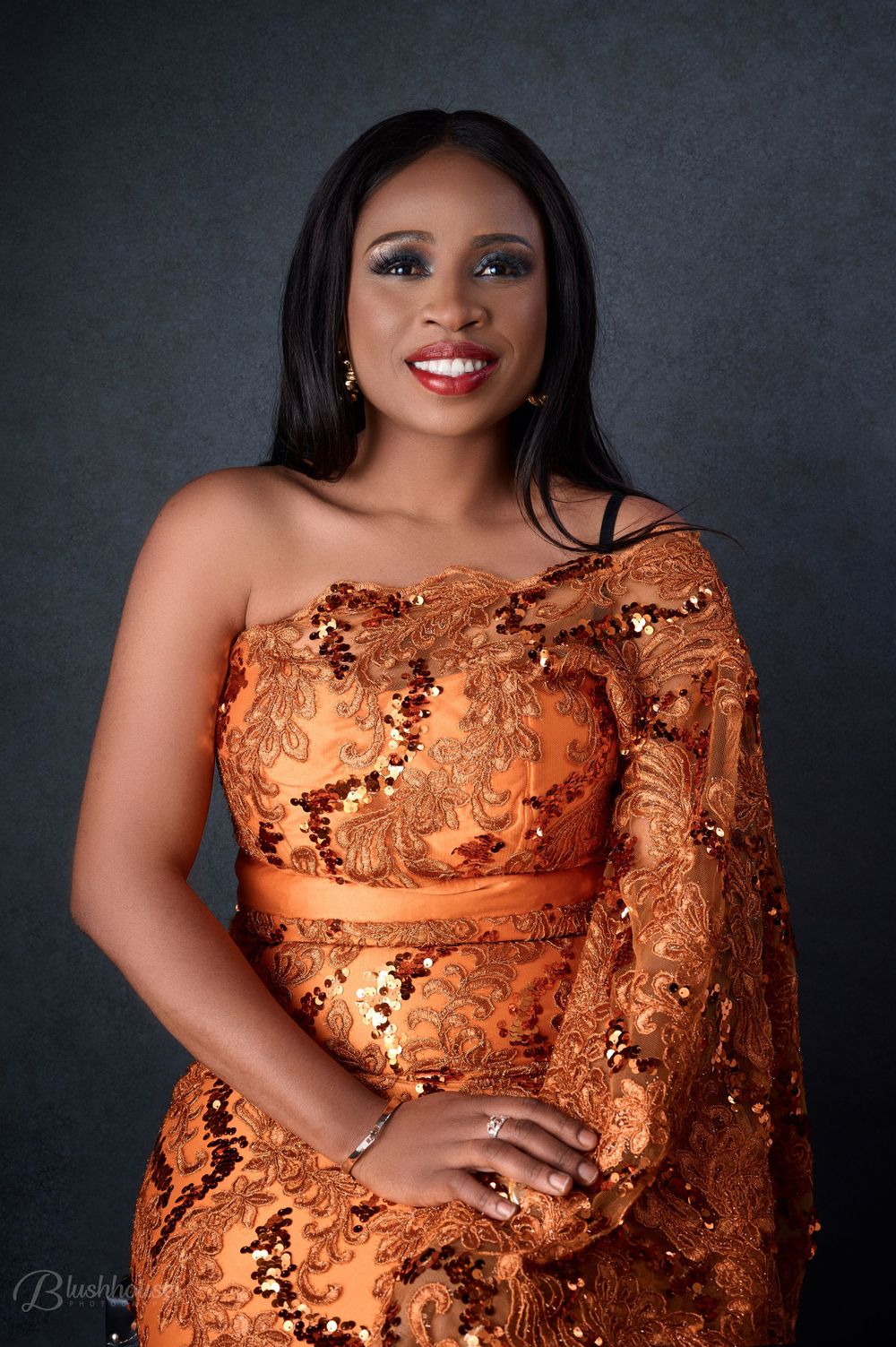 Studio portrait of woman wearing copper-colored lace formal dress against dark background.