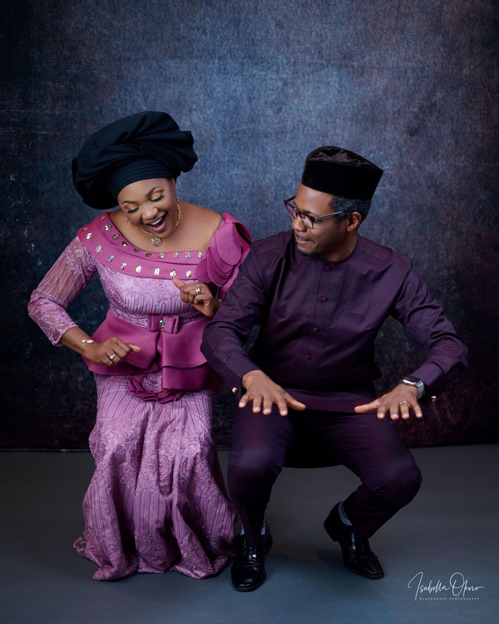 Couple in traditional attire share joyful moment during studio photoshoot against dark backdrop.
