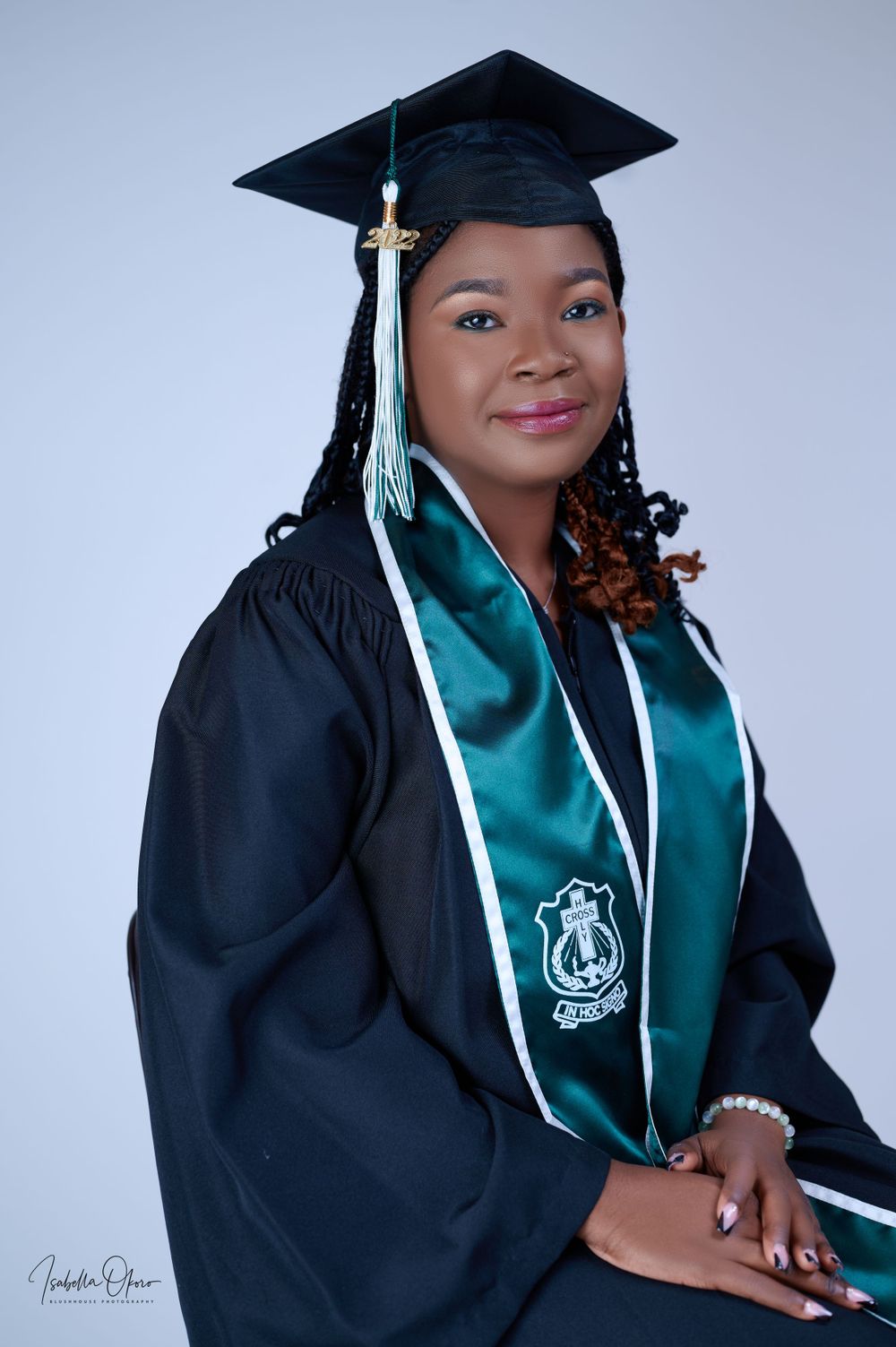 Professional graduation portrait featuring black cap and gown with teal sash against light background.