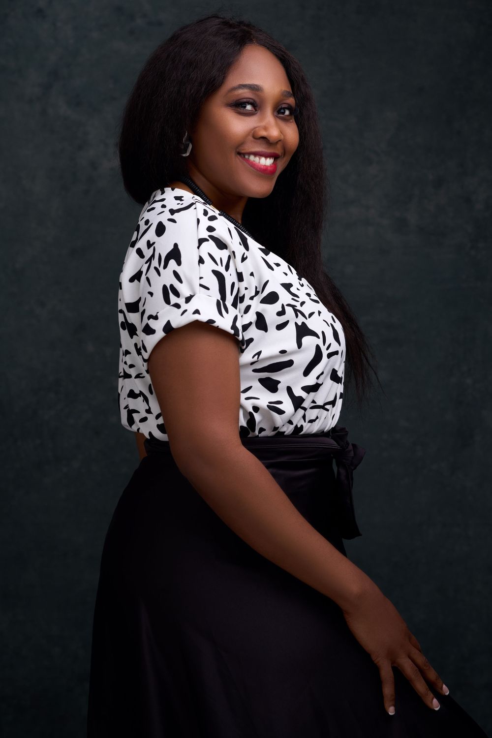 Portrait of woman in black and white patterned top smiling against dark background.
