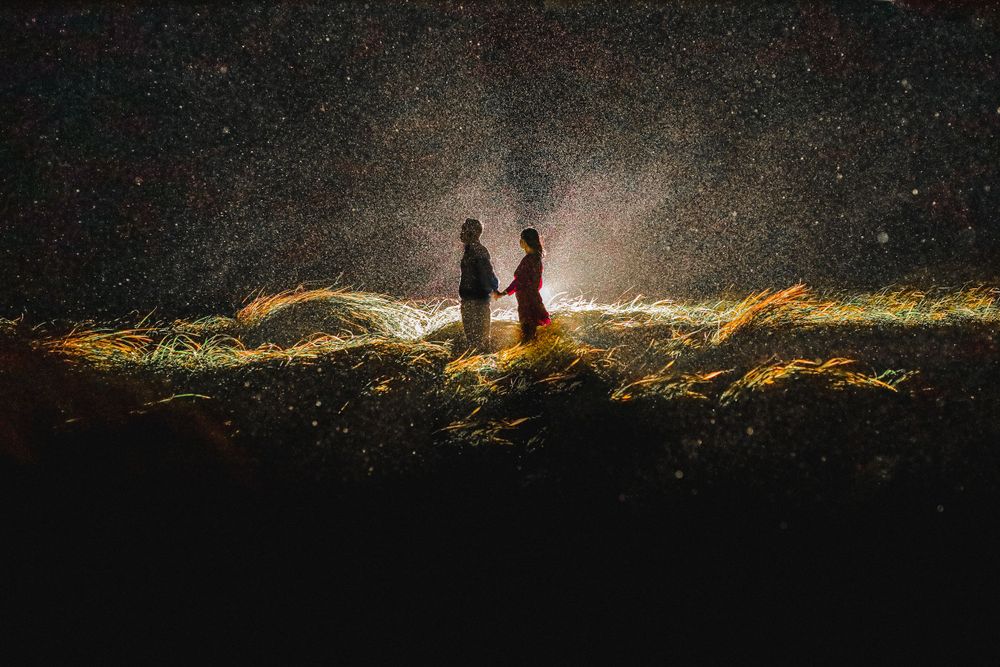 Two silhouettes face each other on a glowing hilltop under a dramatic starry night sky.