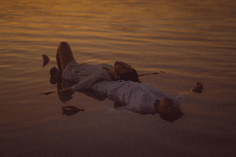 Person floating peacefully on calm golden water at sunset in white clothing.