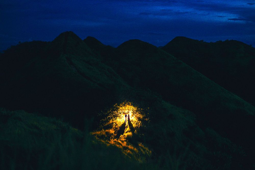 Glowing illuminated tent on dark mountain ridge at night in scenic landscape.