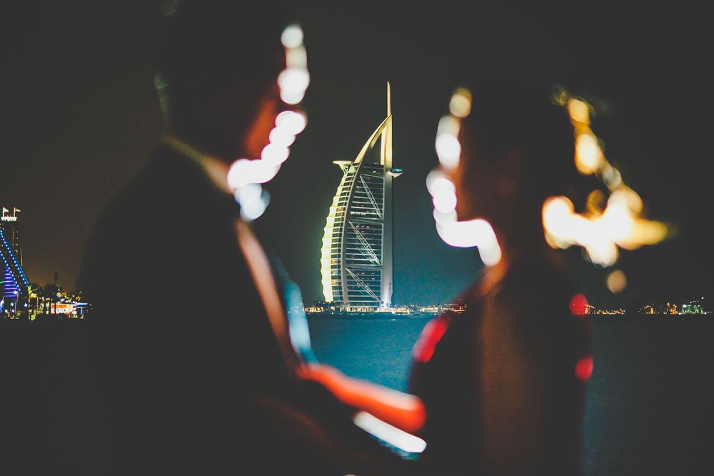 Couple silhouetted against iconic Burj Al Arab hotel at night in Dubai.