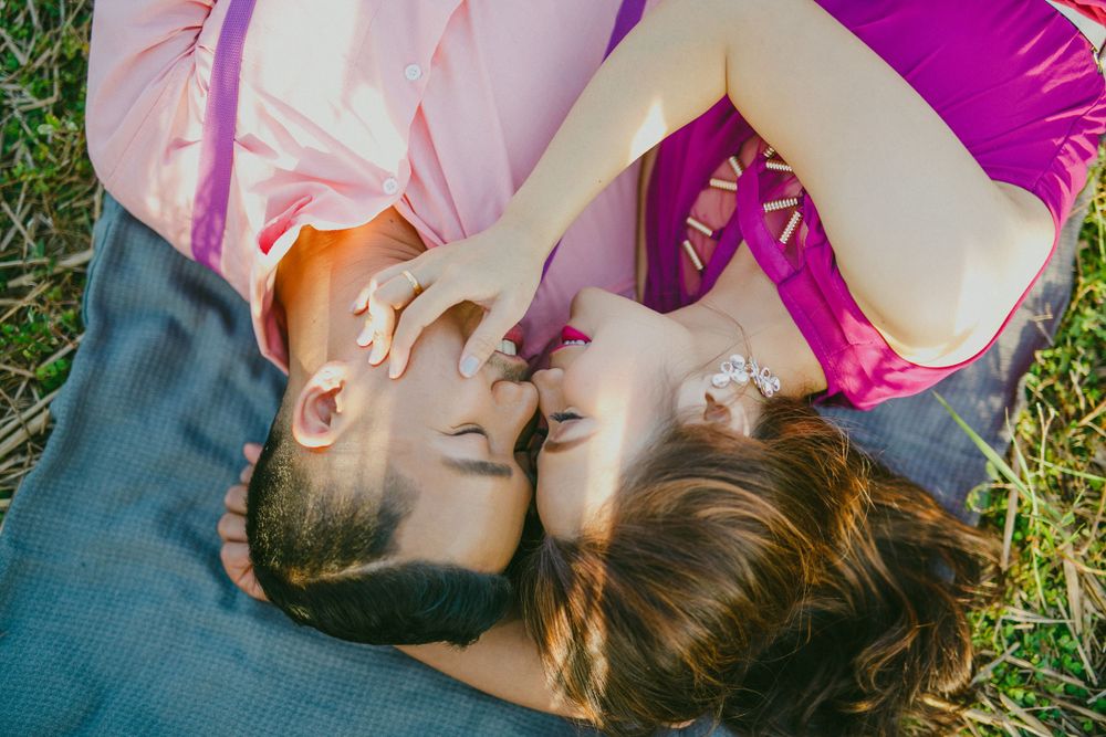Romantic couple lying on grass sharing a tender kiss from above.
