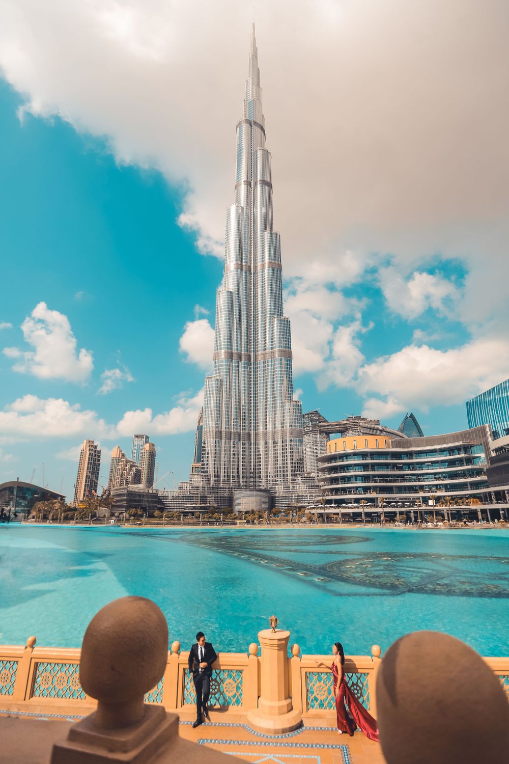 A couple poses near a reflective pool with the iconic Burj Khalifa skyscraper towering behind them in Dubai.