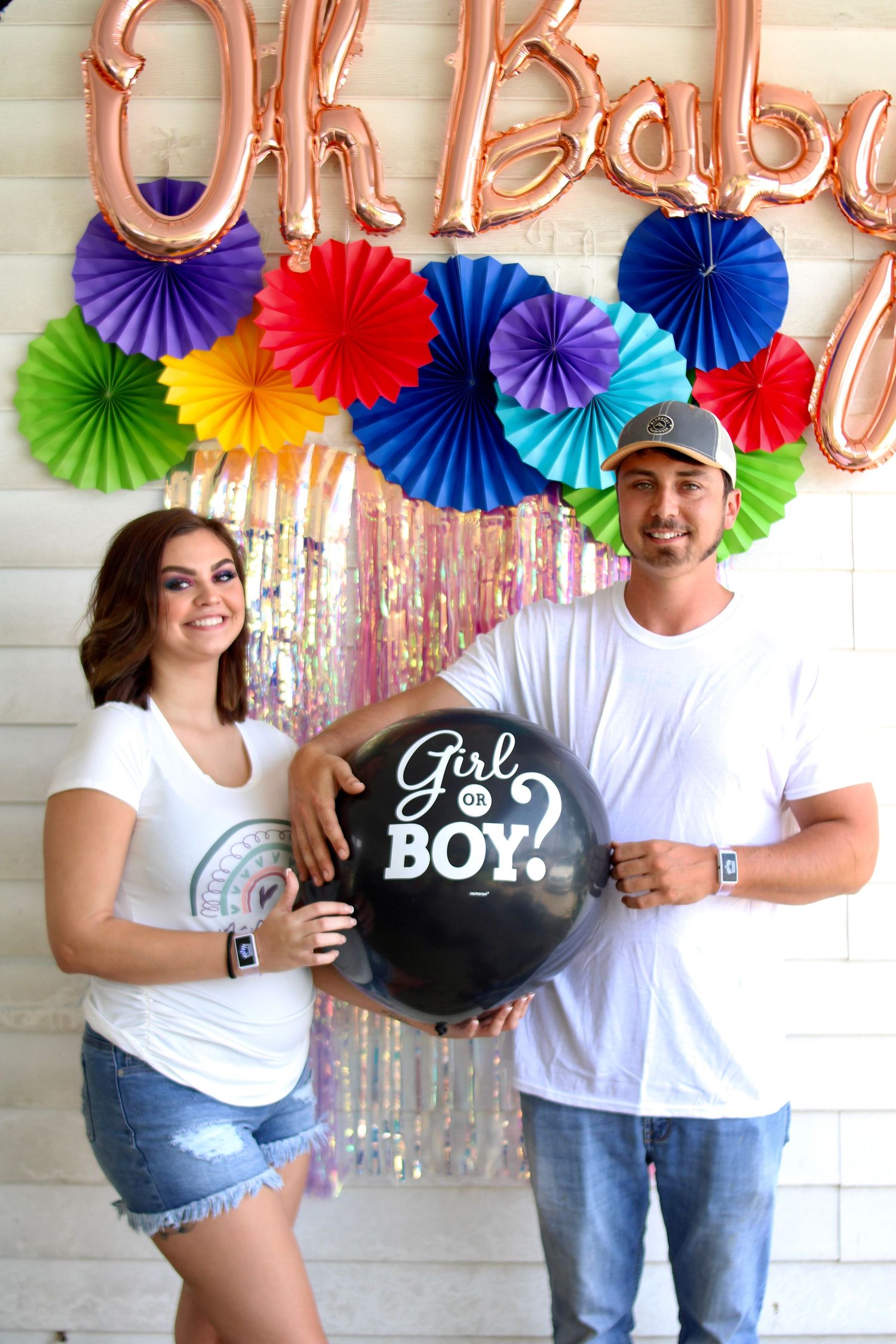 Colorful paper fan decorations and balloons adorn a wall for a gender reveal party.