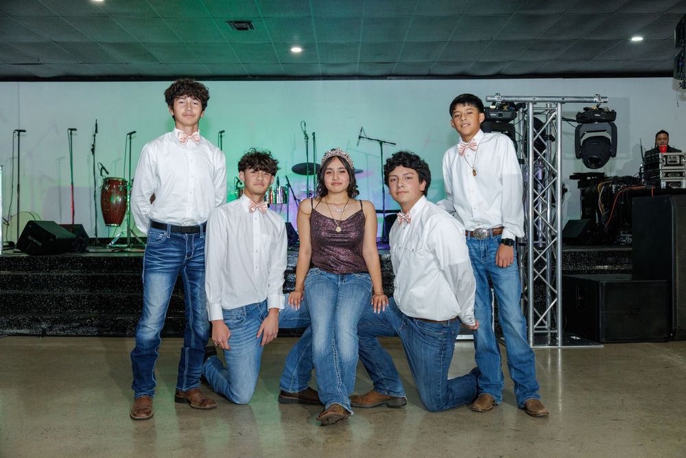 Group photo of five people in western attire posing on stage with music equipment in background.