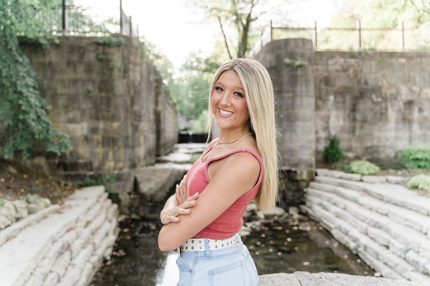 Springfield High School senior in jeans and a muted pink top smiling on the bridge at Side Cut Metropark in Maumee, Ohio.