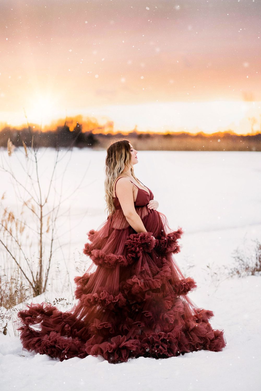 Silhouette of pregnant woman in burgundy dress against winter sunset.