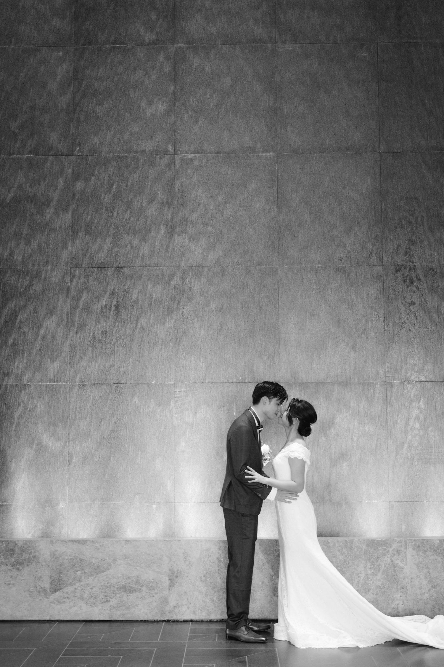 Artistic black and white wedding portraits against a textured concrete wall.