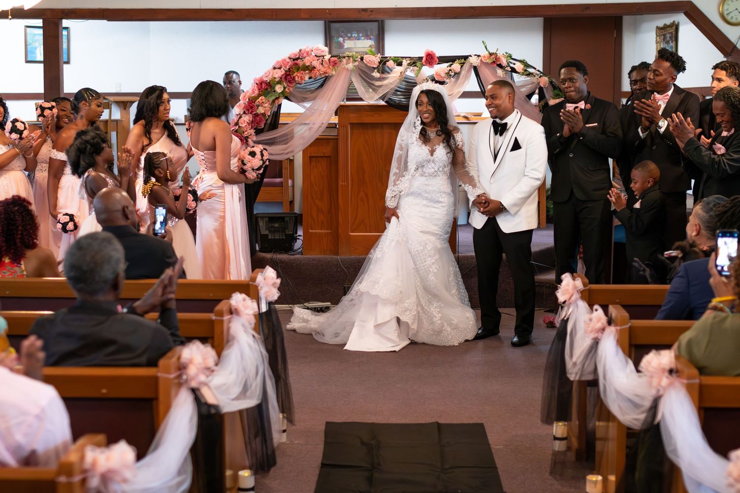 A joyous wedding exit as guests line the church aisle holding raised hands while a couple walks through.
