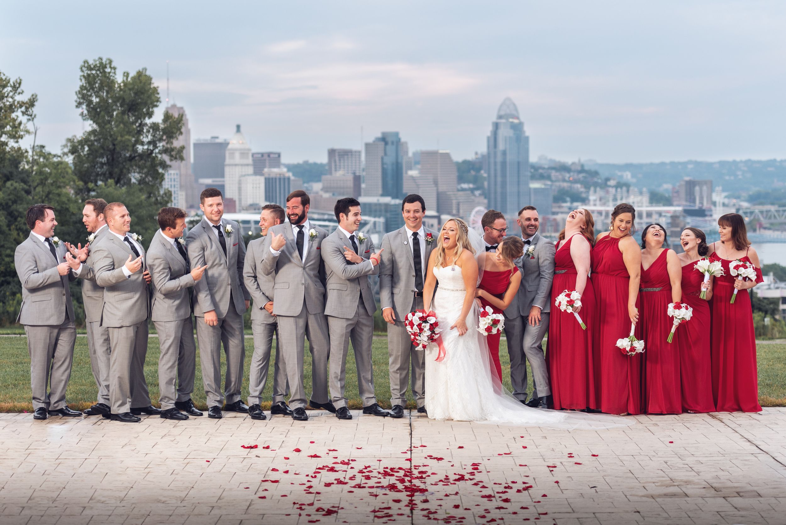 Wedding party poses against city skyline backdrop with red and gray color scheme.