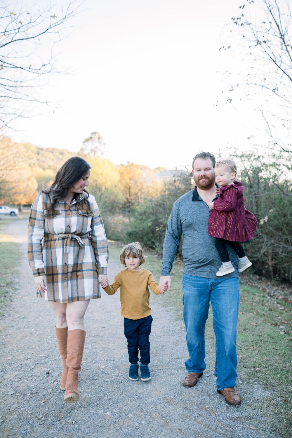 Family walking together on dirt path during golden hour with fall foliage in background.