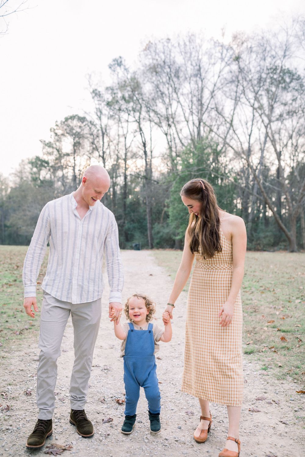 A family holds hands while walking together in a grassy field at sunset.