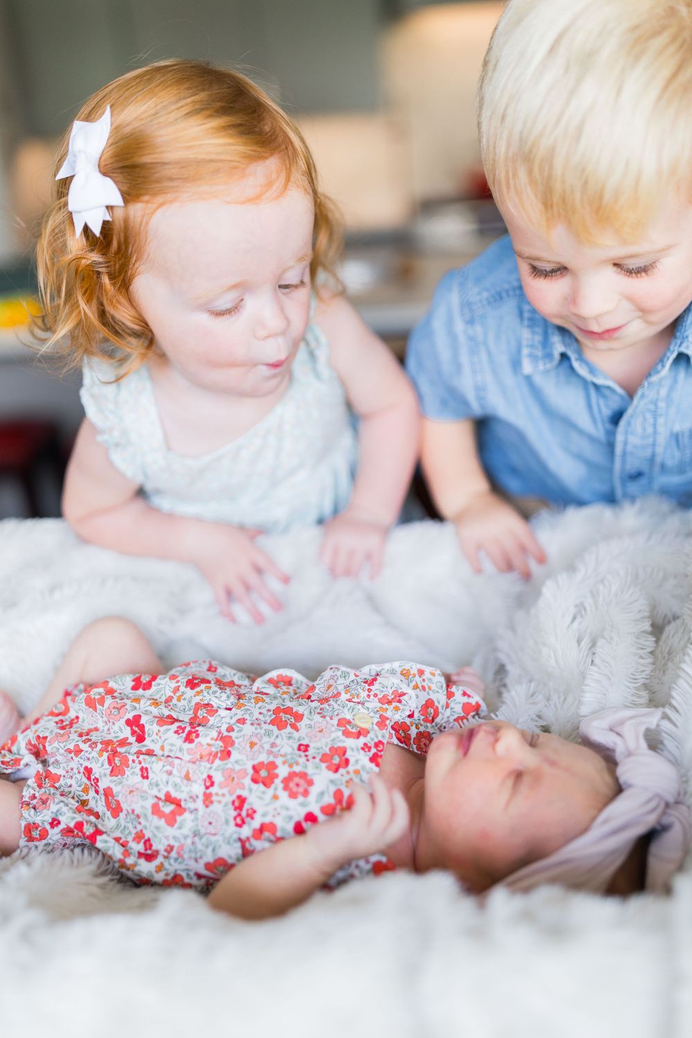 Two young children in blue and white outfits lean over to look at something together on a soft white surface.