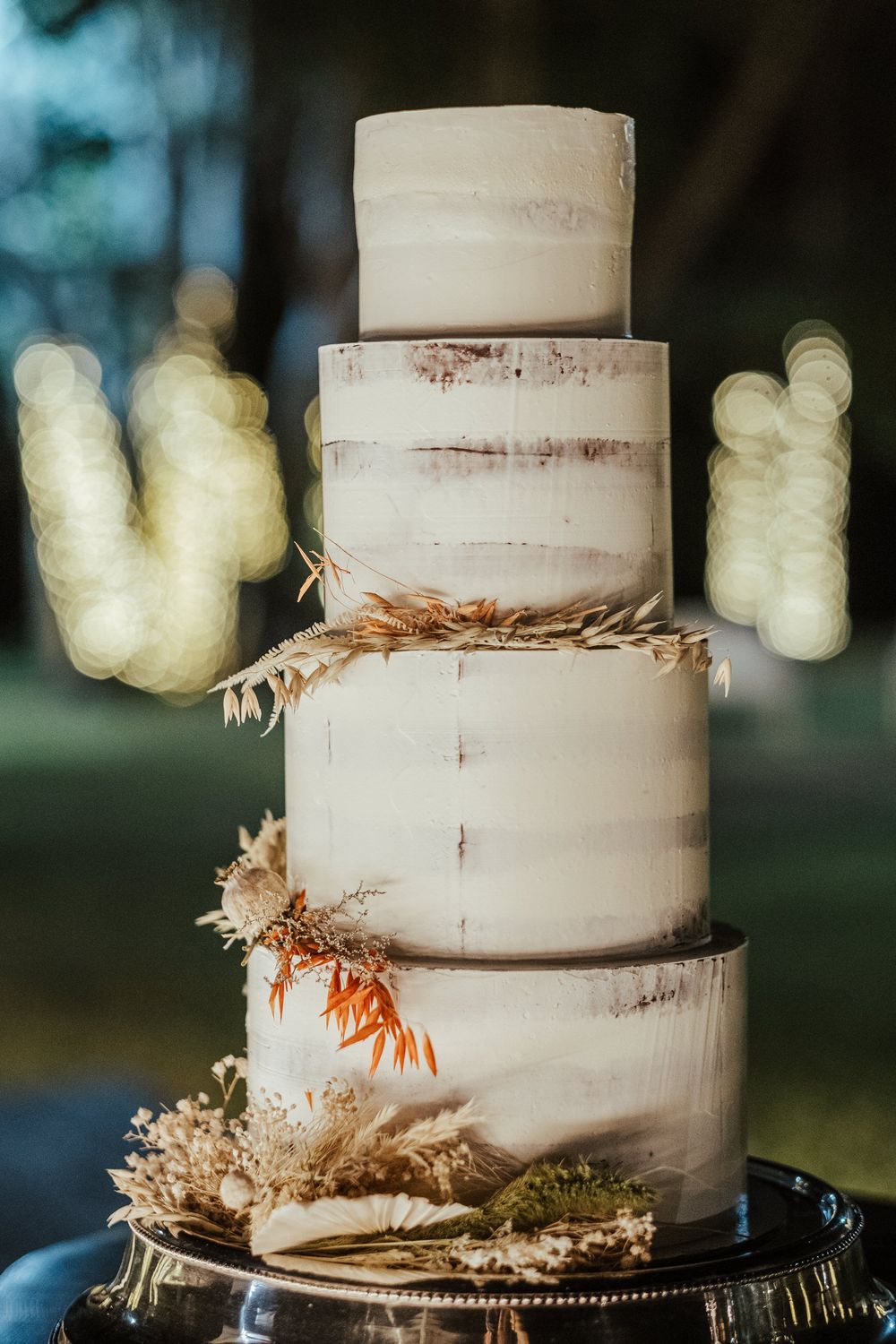 Bolo de casamento branco de três andares, decorado com flores secas e elementos botânicos.