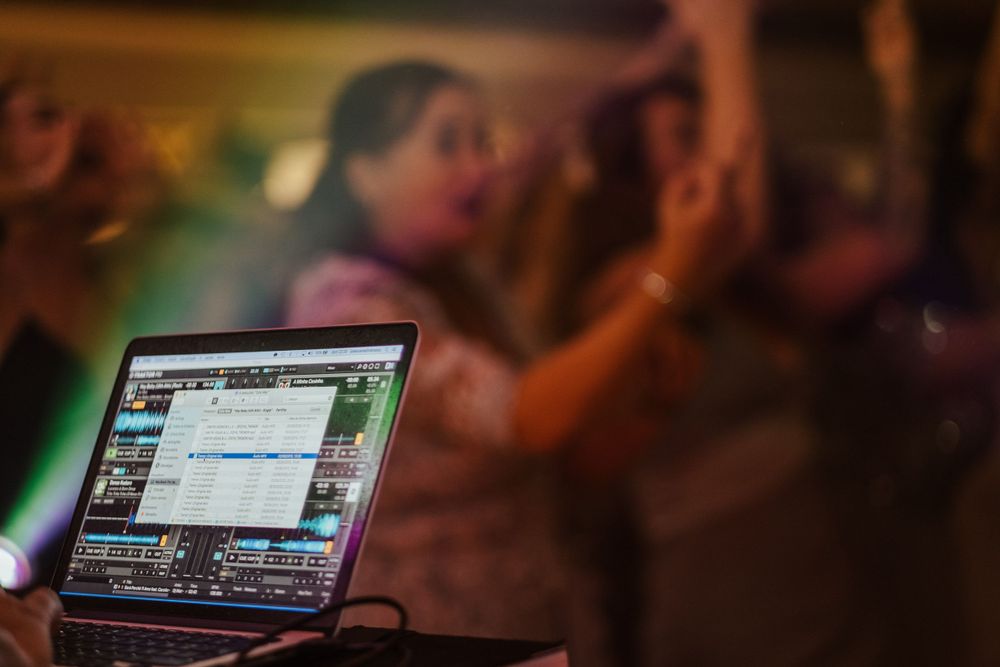 Configuração do portátil de DJ num evento numa discoteca, com a multidão da festa desfocada ao fundo.