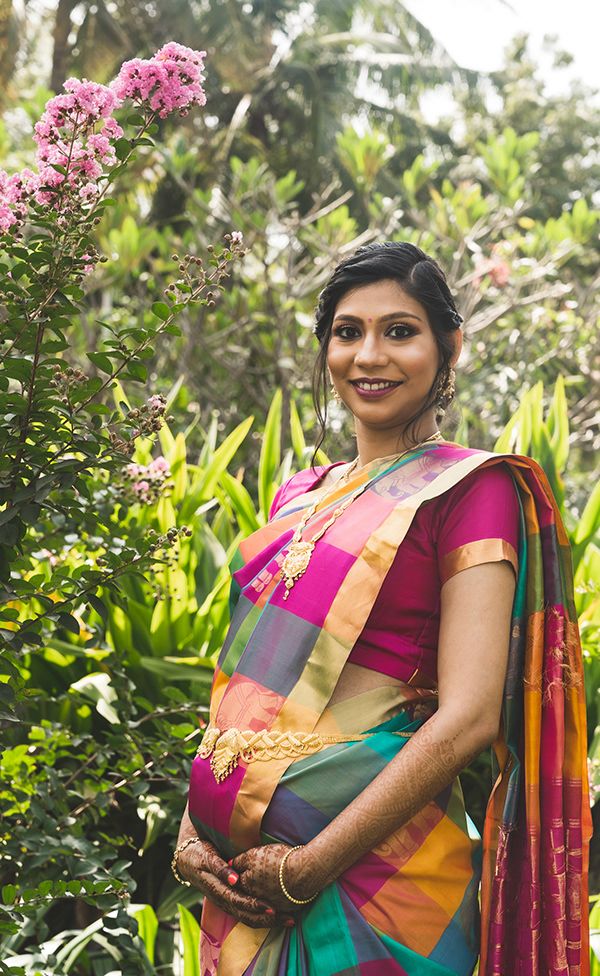 A traditional South Indian silk sari adorns the figure posing by pink flowers in a garden setting.