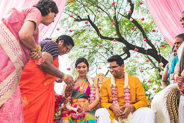 Celebratory moment during outdoor Indian wedding with family gathered under pink canopy.