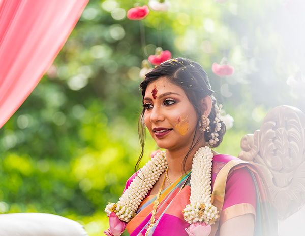 Traditional South Indian bride adorned with jasmine flowers and jewelry against a natural backdrop.