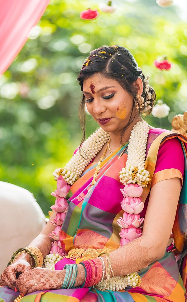 Traditional Indian bride wearing pink silk saree and jasmine flower garlands during wedding ceremony ritual.