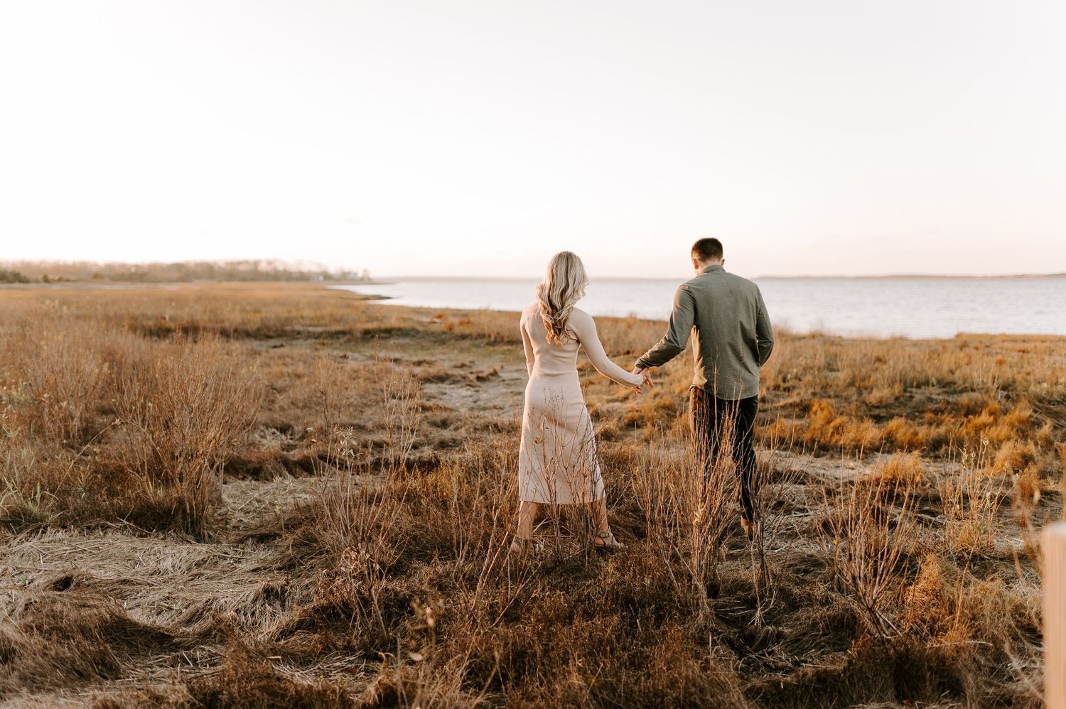 Two people walk together across a scenic coastal field at sunset.