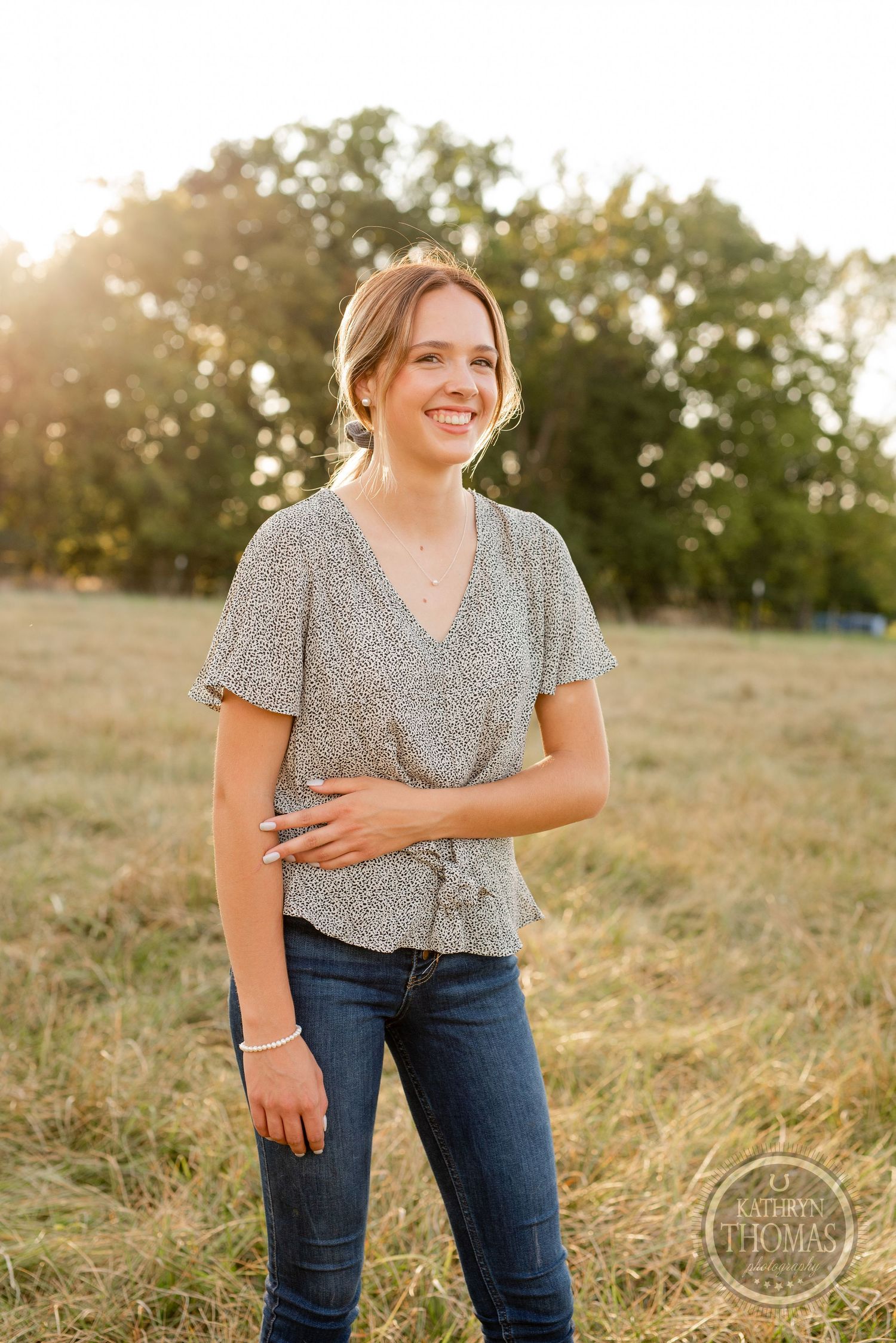 Portrait in a floral top against golden sunset light in open field.