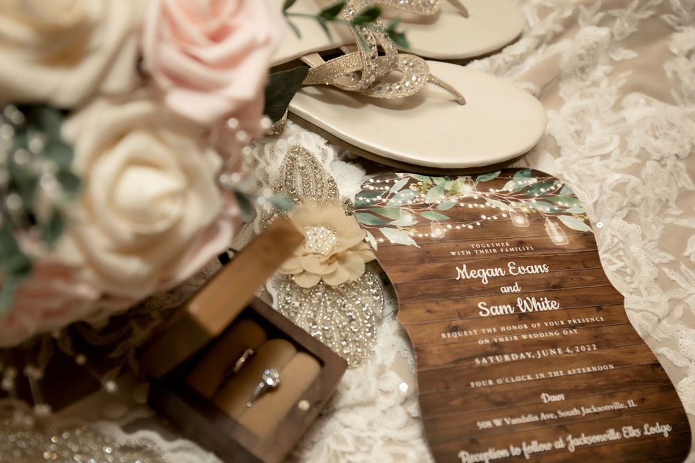 Wedding details with rings and wooden invitation among blush roses.