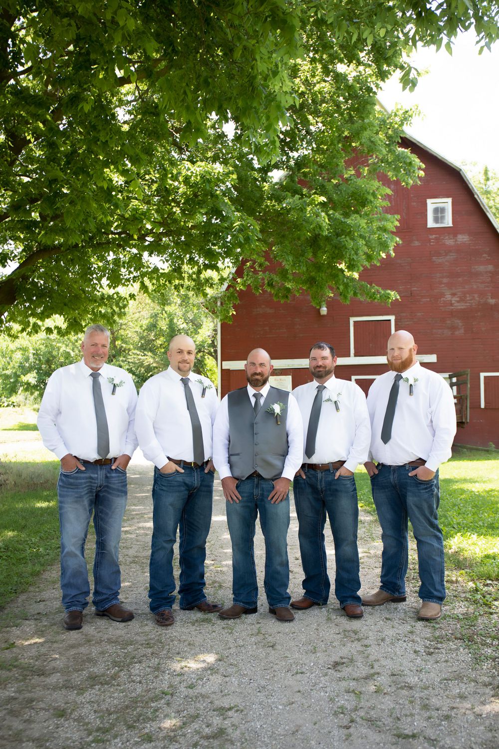 Groomsmen in casual attire pose in front of red barn wearing white shirts and jeans.