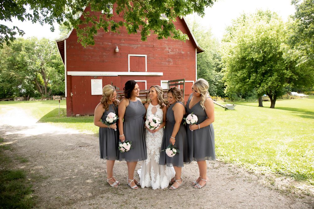 Bridal party in grey dresses poses in front of red barn.