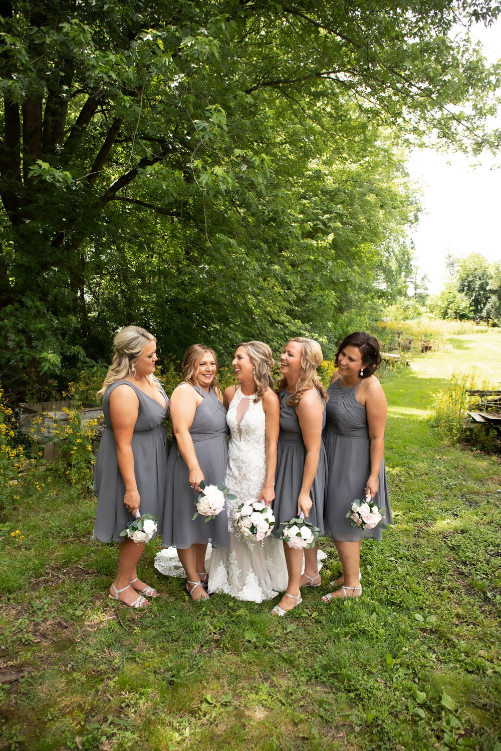 Wedding party with bridesmaids in grey dresses gather in garden setting.