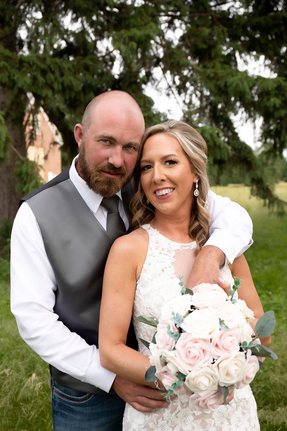 Newlywed couple poses together outdoors holding pink and white rose bouquet.