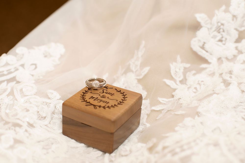 Wedding rings rest on wooden box atop delicate lace fabric.